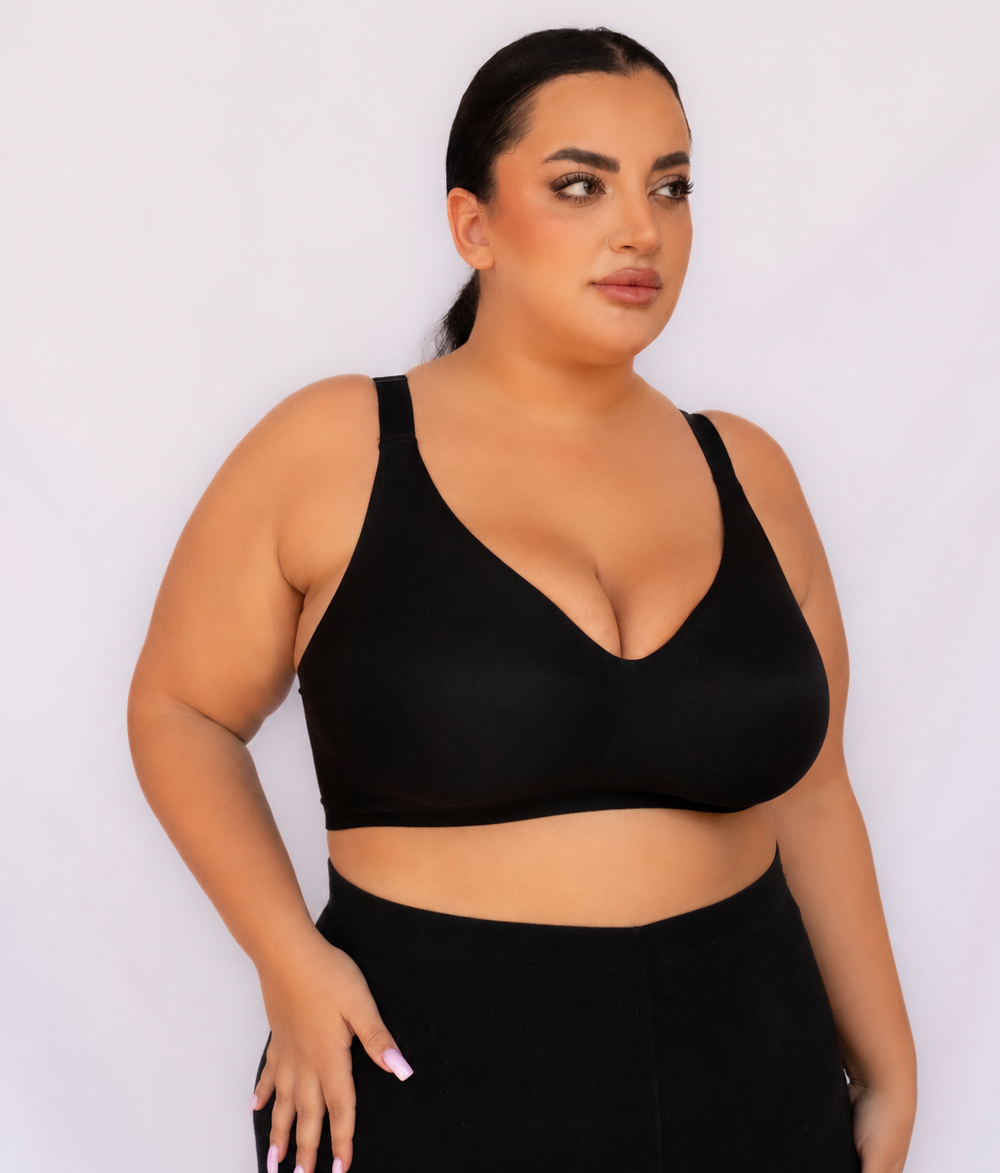 A plus-size woman wearing a black wireless scoop-neck crop top and matching black high-waisted leggings, posing against a light gray studio background.