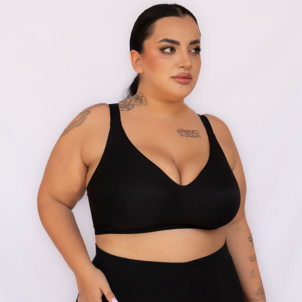 A plus-size woman modeling a black wireless bralette and matching black high-waisted leggings against a plain white studio background.